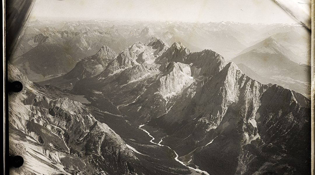 Schwarzweiße Luftbildschrägaufnahme eines Gebirges.