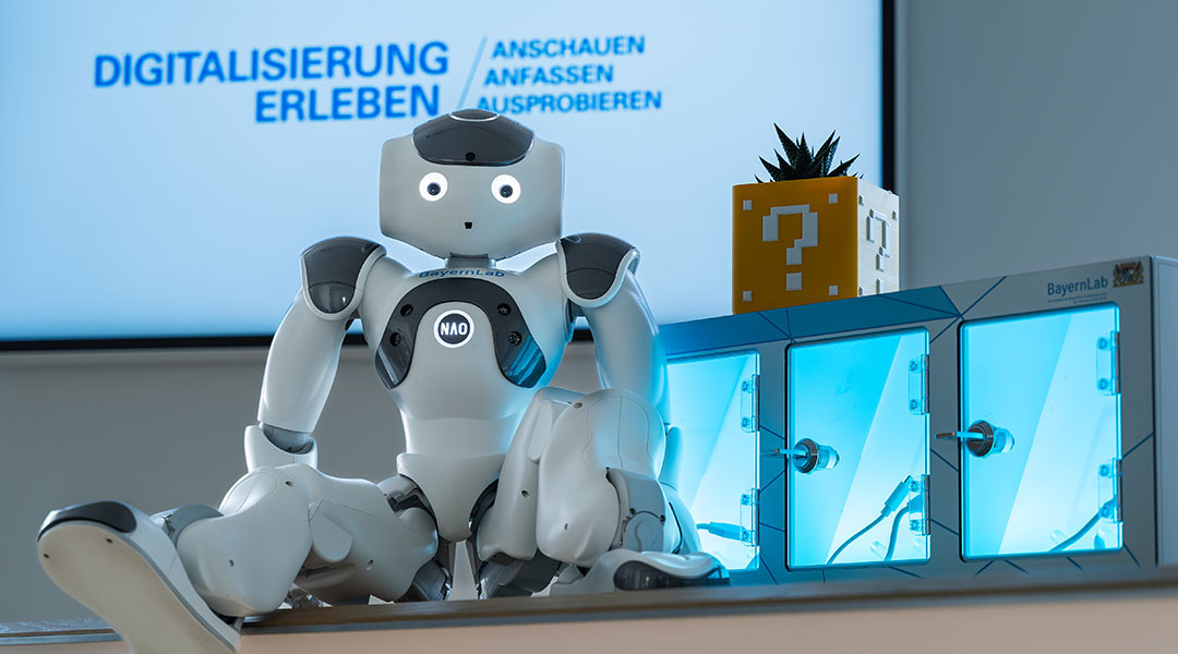 Der Roboter NAO sitzt im BayernLab Forchheim vor einem Bildschirm, auf dem 
